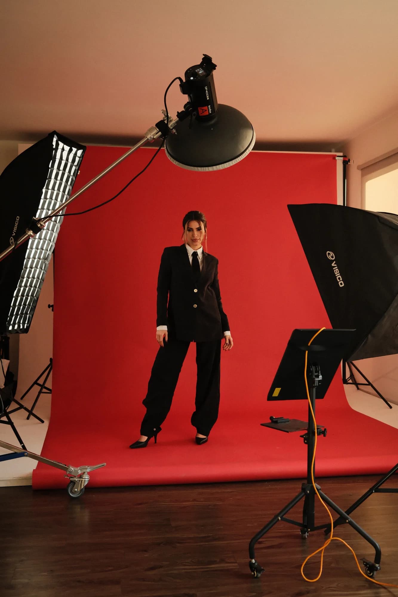 Modelo de traje negro parada sobre el fondo rojo del estudio, entre flashes y softbox