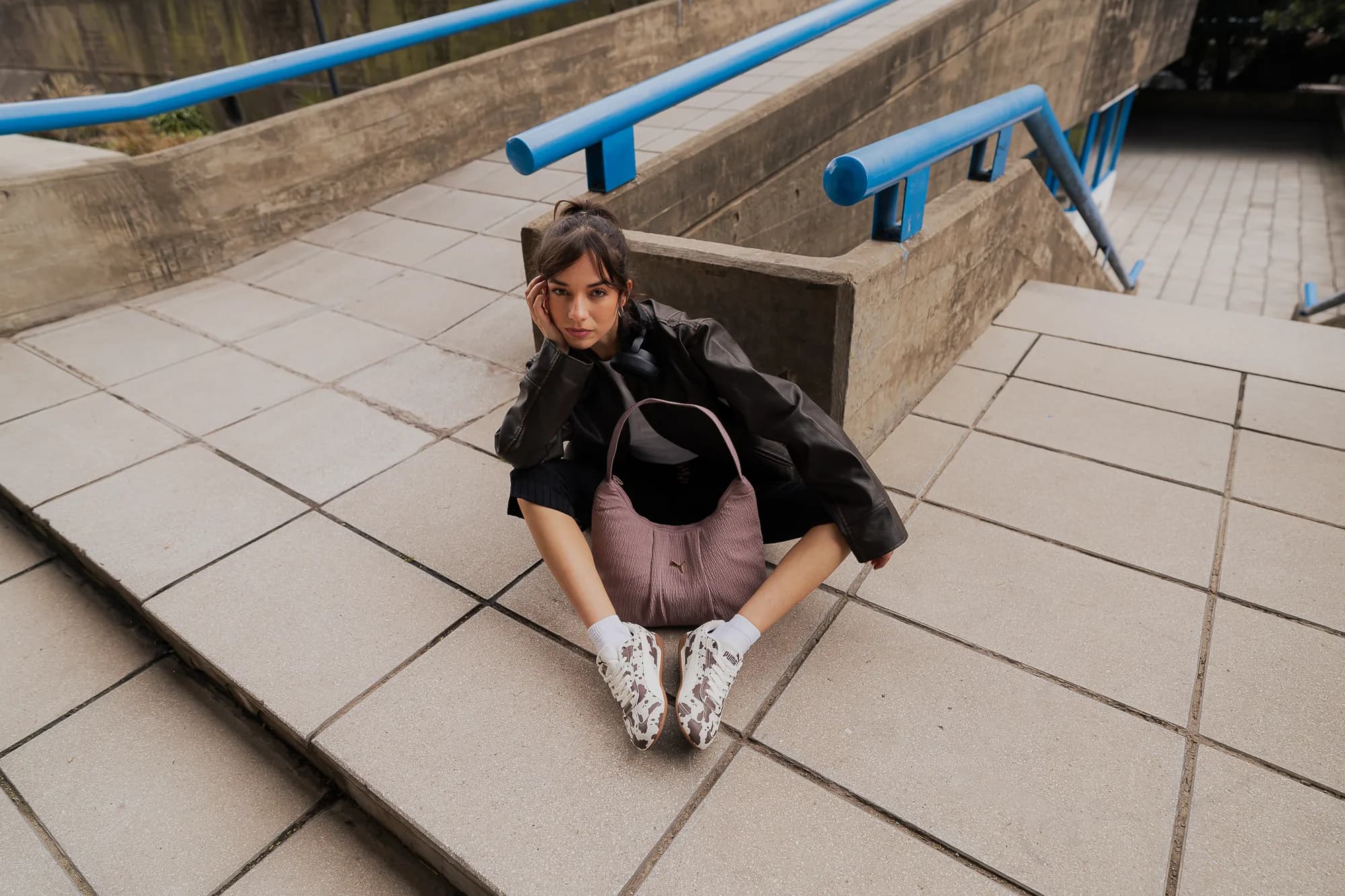 Modelo sentada en una escalera de cemento con barandas azules, mirando a cámara